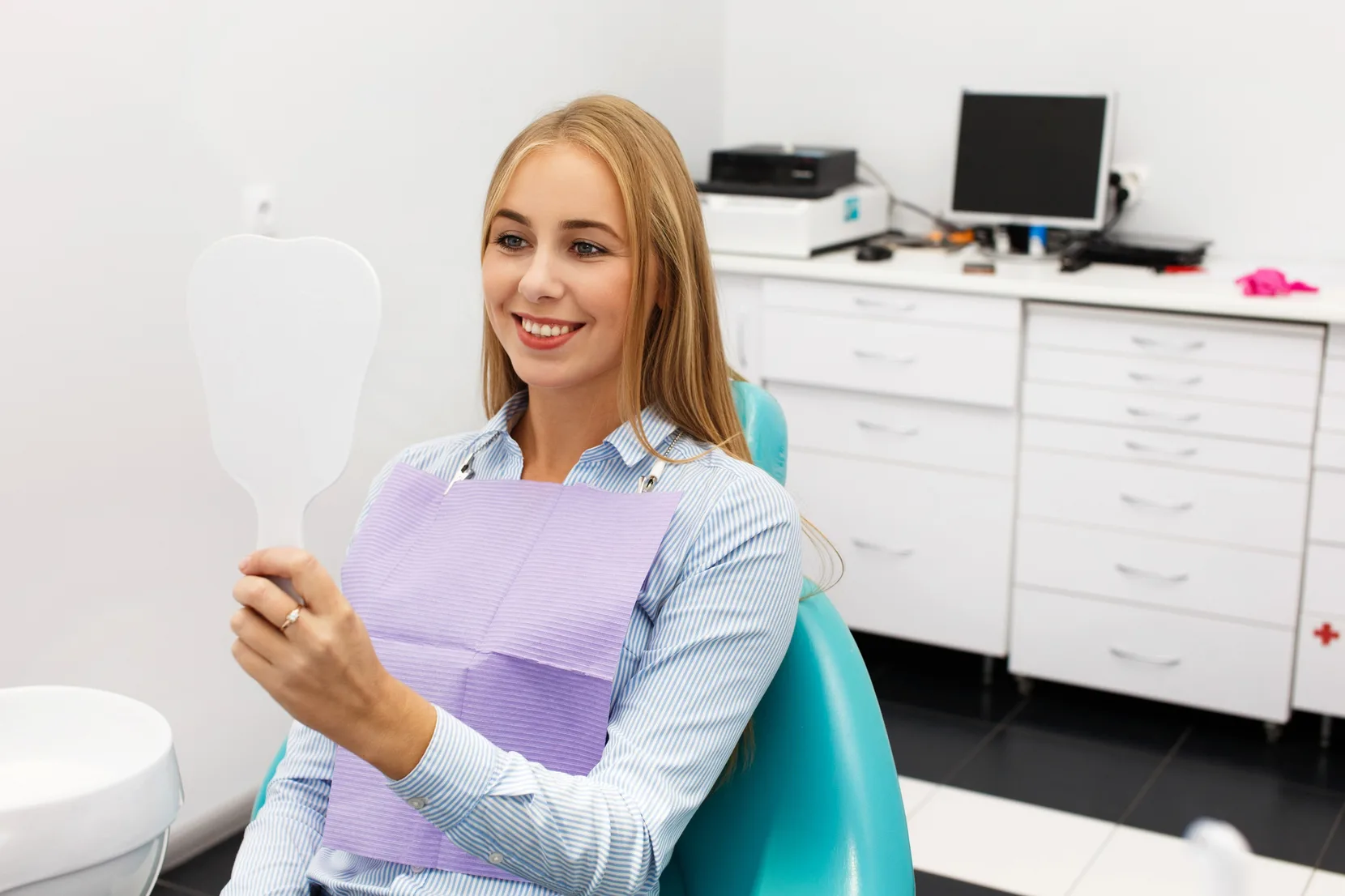 Patient smiling at her new teeth in a hand mirror